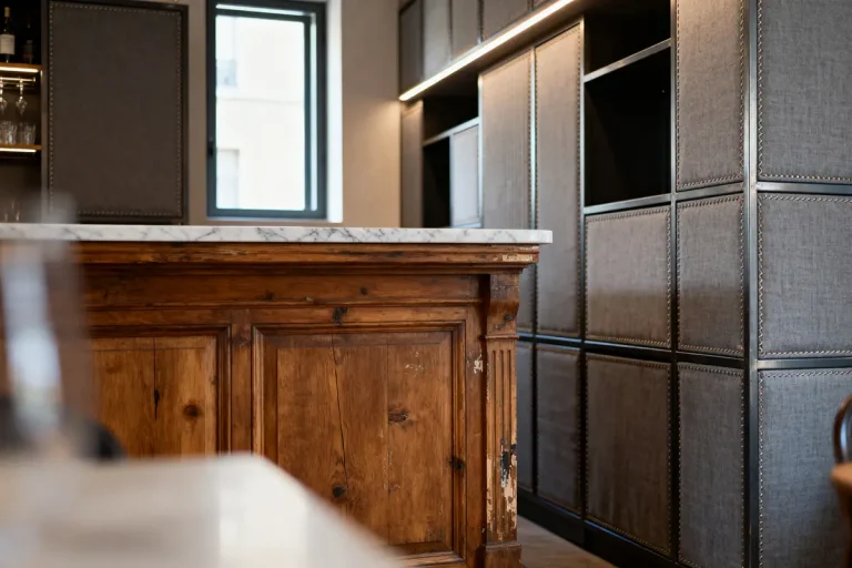 Cuisine moderne avec îlot en bois massif, plan de travail en marbre, étagères grises et éclairage intégré.