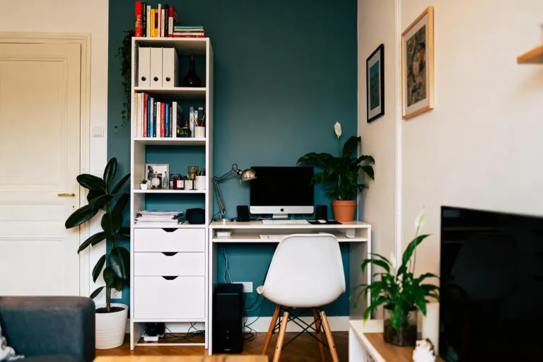Bureau à domicile moderne avec chaise, ordinateur, étagère pleine de livres et plantes dans un intérieur cozy.