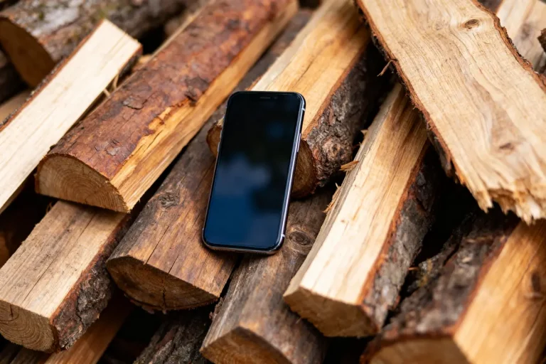 Smartphone sur des bûches de bois, écran éteint, dans un environnement extérieur.