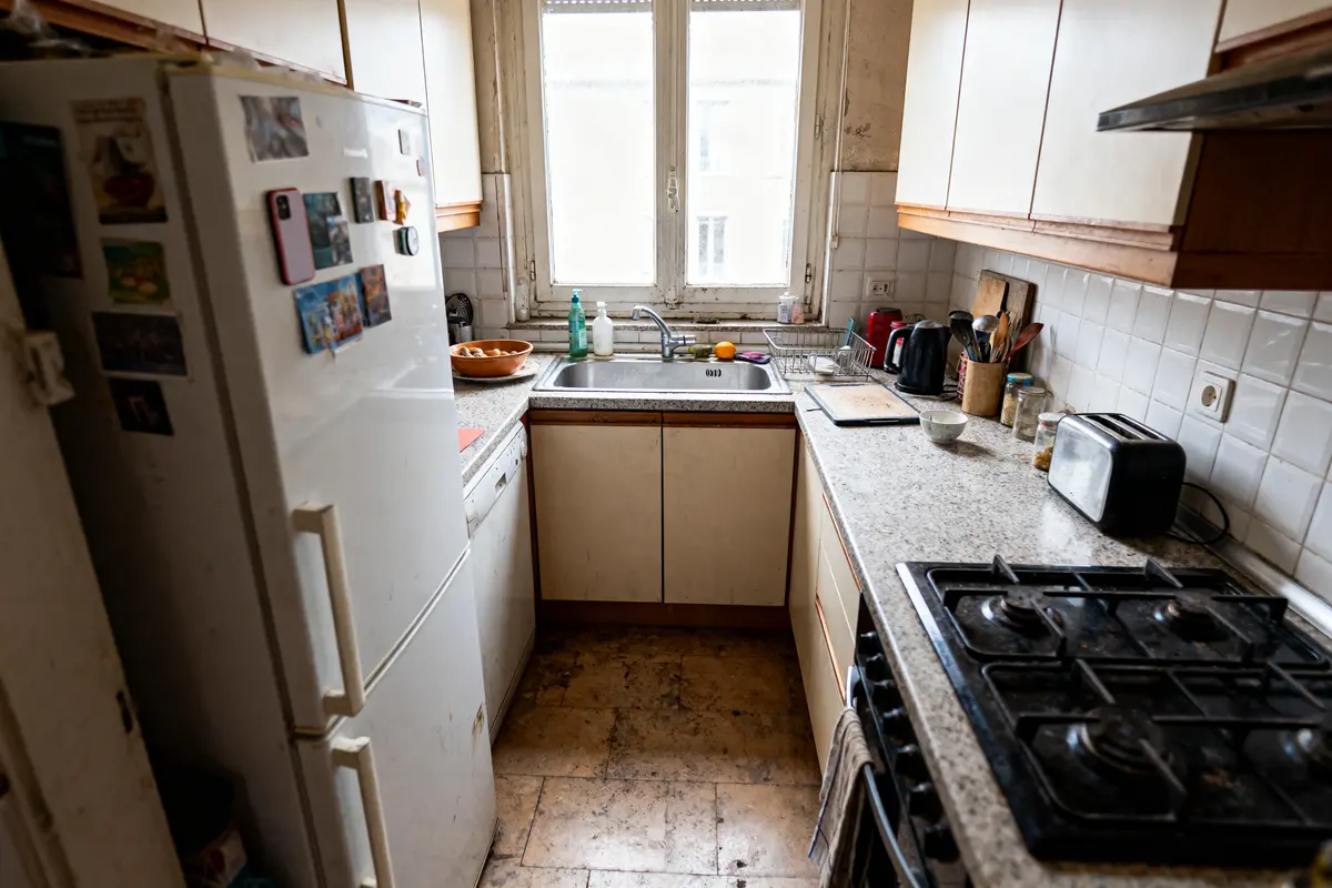 Cuisine étroite avec électroménagers, planches à découper, évier, réfrigérateur et fenêtre lumineuse.