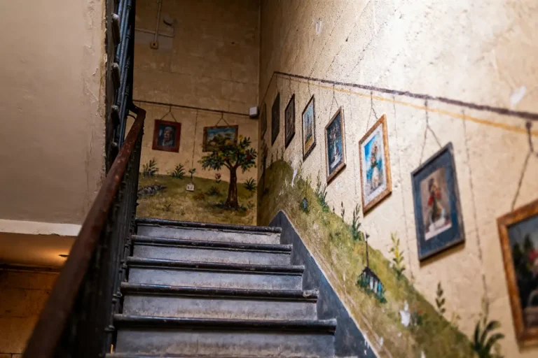 Escalier peint avec fresque murale illustrant nature et plusieurs tableaux encadrés suspendus sur les murs.
