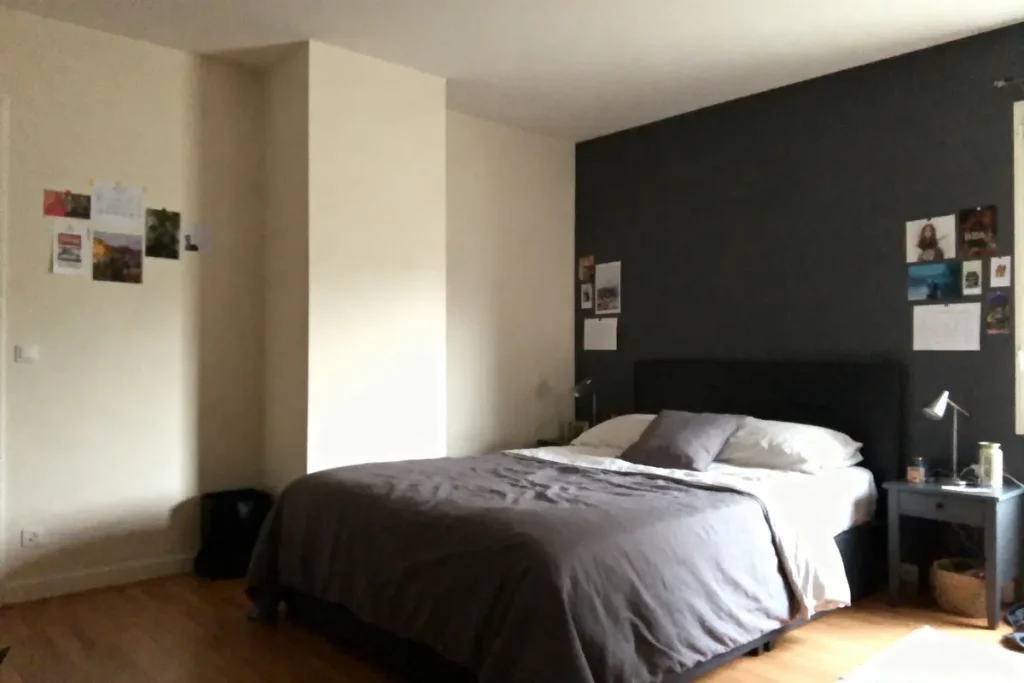 Chambre avec lit double, couvre-lit gris, mur sombre, lampes, photos décoratives, sol en bois.