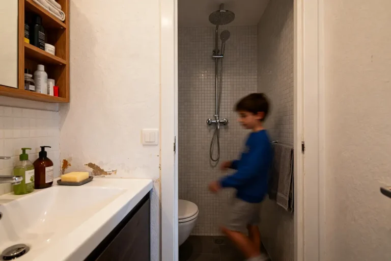 Petite salle de bain avec douche, lavabo moderne, murs carrelés, et enfant flou en mouvement.