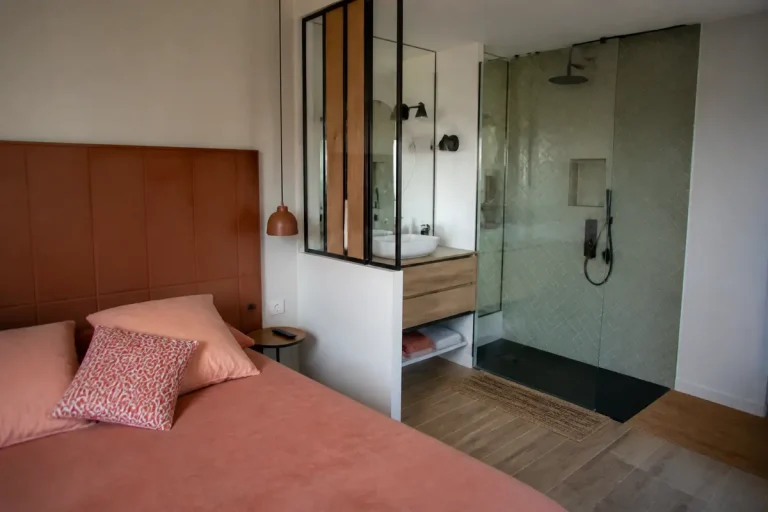 Chambre moderne avec lit double, douche vitrée, lavabo et lampe suspendue, ambiance chaleureuse et accueillante.