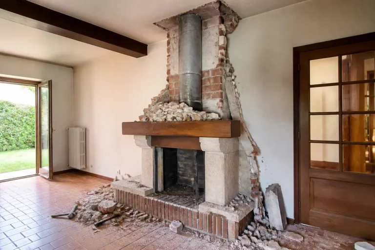 Cheminée en cours de rénovation dans un salon vide, murs en brique, baies vitrées.