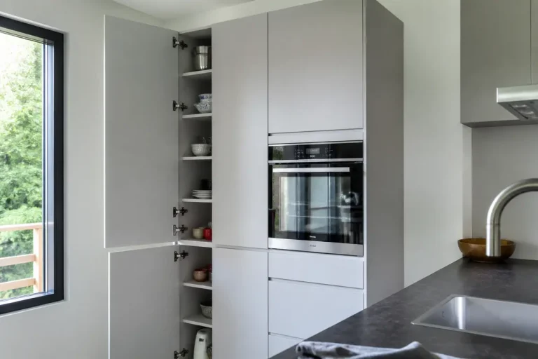 Cuisine moderne avec placard ouvert, four encastré, fenêtre à gauche et lavabo au premier plan.