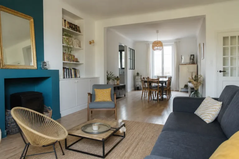Salon moderne avec canapé, fauteuils, table basse, cheminée, étagères, coin repas, décoration épurée et lumineuse.