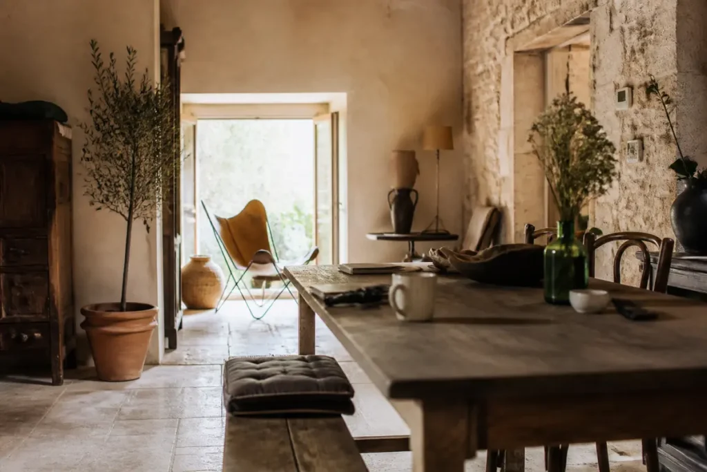 Intérieur de maison avec table rustique, plantes, éclairage naturel, chaise moderne près de la fenêtre ouverte.