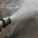 Gros plan d'un tuyau d'incendie projetant de l'eau sur une surface mouillée.