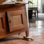 Un meuble en bois calé avec des livres pour stabiliser ses pieds sur le sol carrelé.