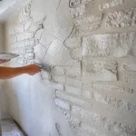 Un homme applique du plâtre sur un mur texturé intérieur, créant un effet pierre décoratif.