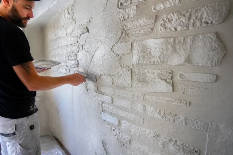 Un homme applique du plâtre sur un mur texturé intérieur, créant un effet pierre décoratif.