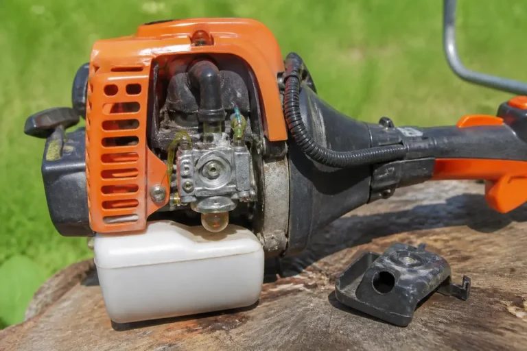 Moteur de débroussailleuse orange posé sur une souche de bois avec fond herbeux flou.