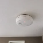Détecteur de fumée installé au plafond avec témoin lumineux rouge allumé.