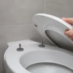 Personne installant un abattant de toilette blanc dans une salle de bain moderne avec carrelage beige.