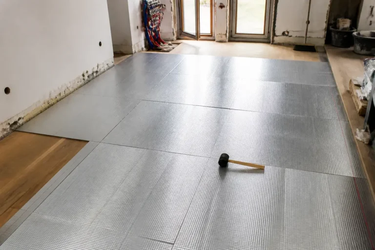 Installation de panneaux isolants au sol dans une pièce avec marteau et parquet visible à gauche.