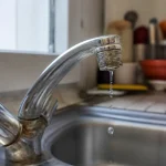Robinet en métal avec goutte d'eau tombant dans un évier de cuisine en acier inoxydable.