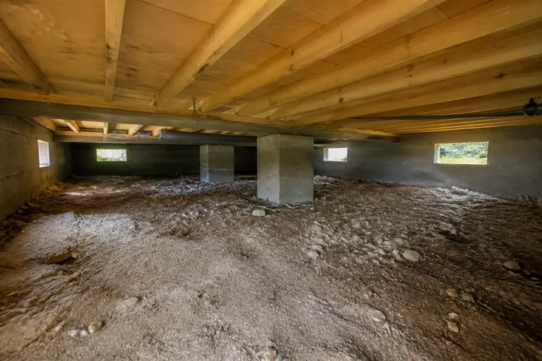 Espace sous une maison avec vide sanitaire, sol en terre battue et piliers béton.