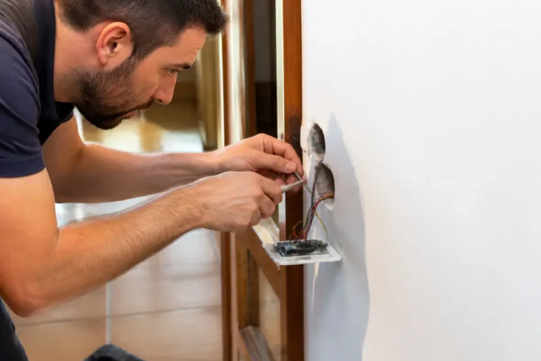 Électricien effectuant des réparations de câblage mural, concentré sur des fils exposés dans une prise électrique.