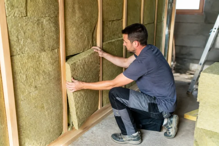 Un homme installe des panneaux d'isolation dans une structure en bois, illustrant l'amélioration énergétique d'une maison.