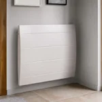 Radiateur moderne blanc fixé au mur dans un intérieur lumineux avec parquet et porte vitrée.