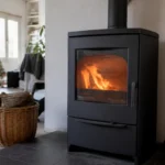 Poêle à bois noir en fonctionnement dans un salon moderne avec parquet et panier de bûches en osier.